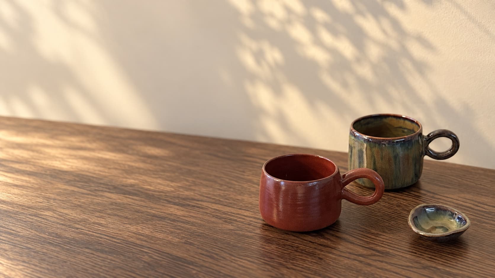 Handmade terracotta and sage ceramic mugs on a wooden table